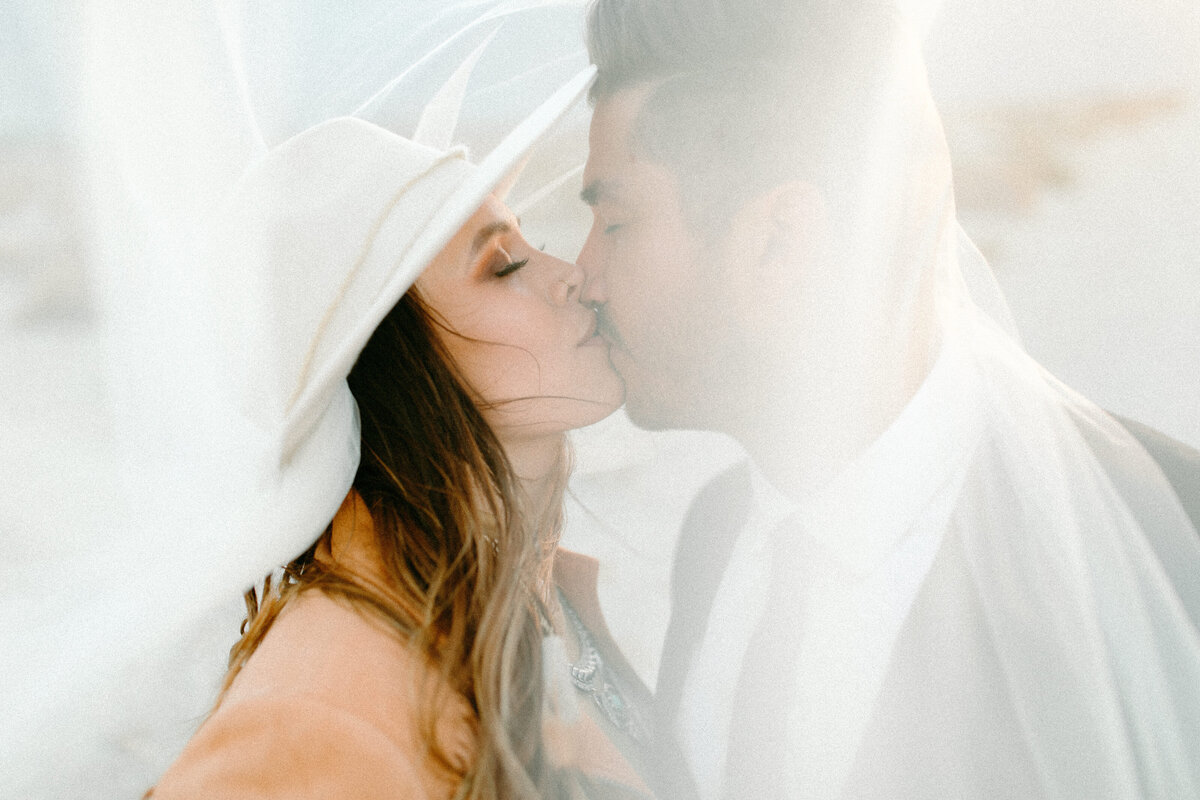 Bride and Groom kissing under a veil with a gust of Texas wind blowing the veil