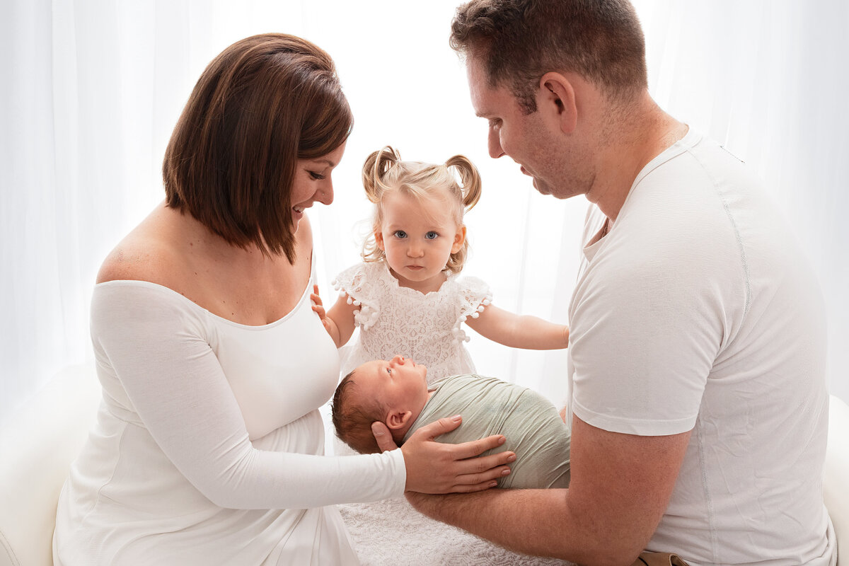 Family holding their newborn in a bright, neutral white Oakville studio portrait