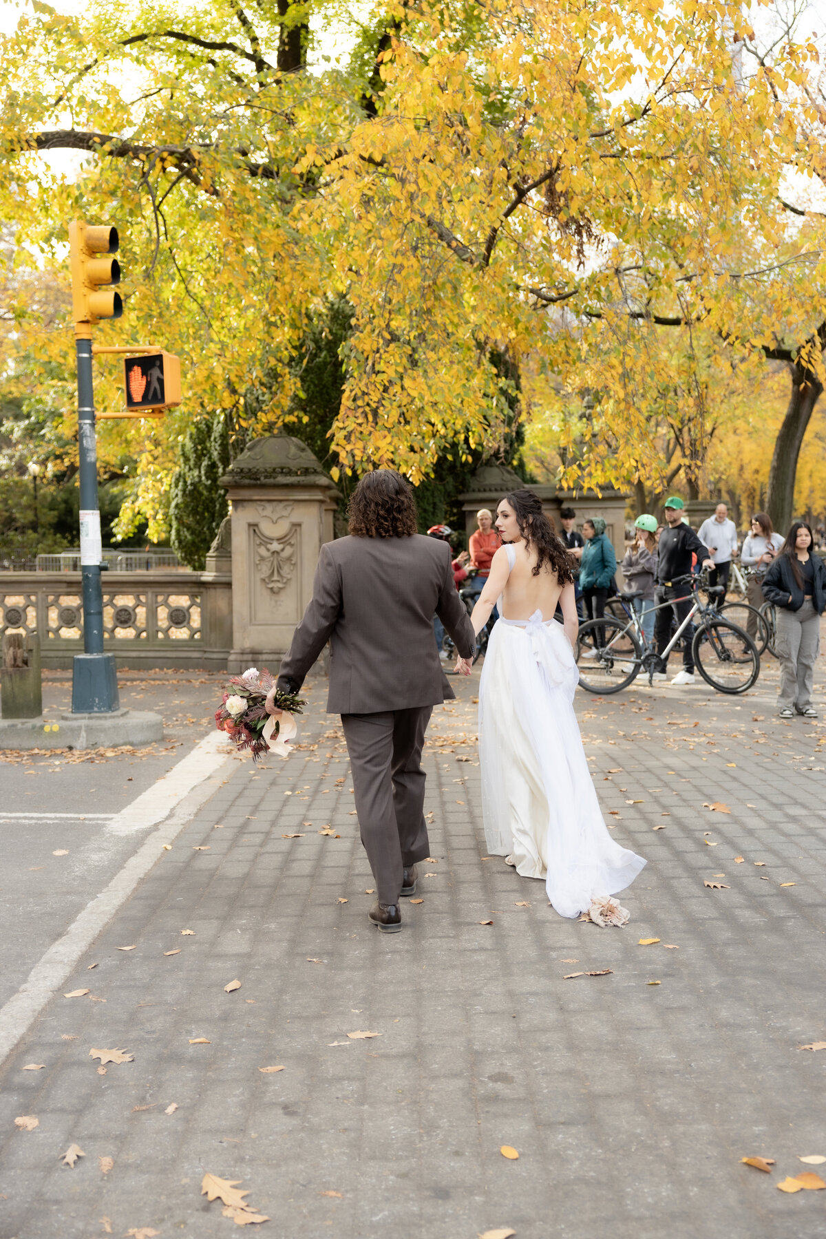 The bride laughing joyfully while holding her bouquet among autumn leaves in Central Park.