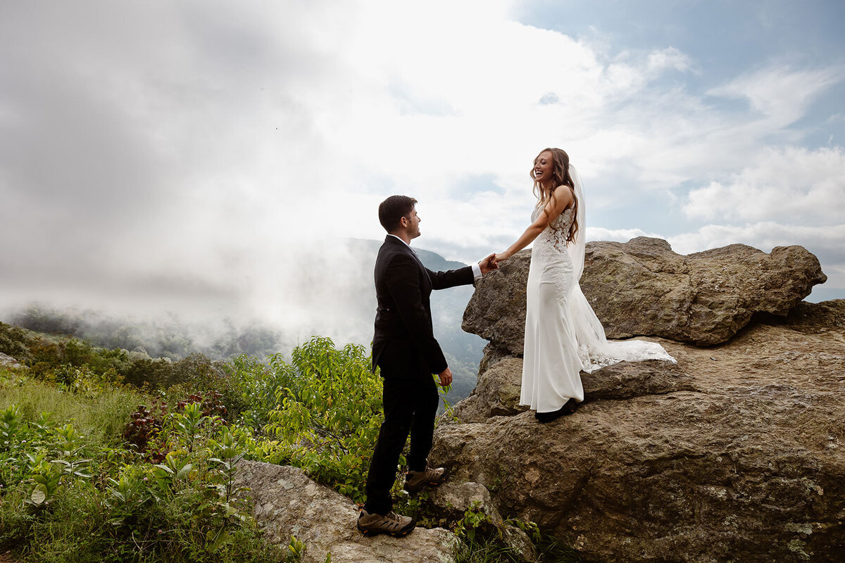 A person helping their partner down from a rock