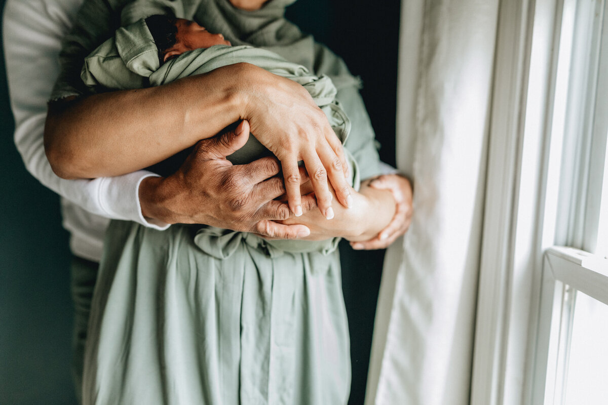 Mom holding new born baby, with dad holding arms around mom.