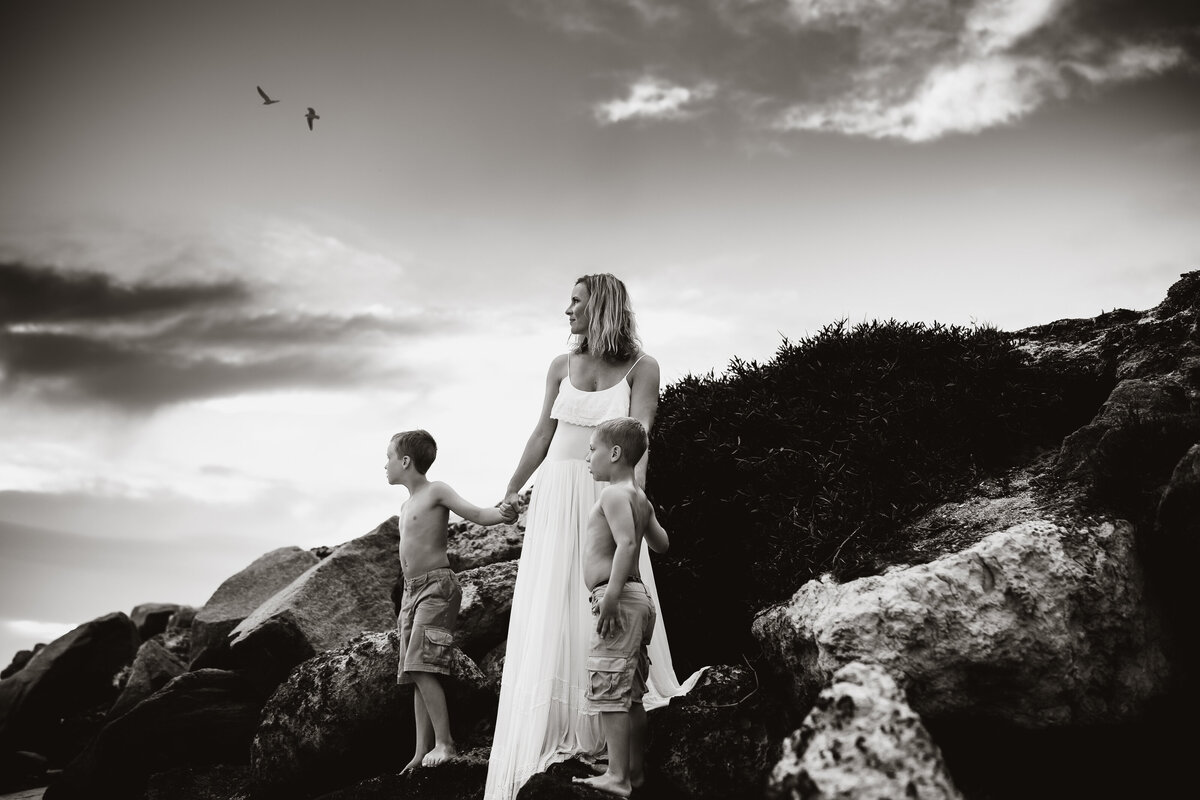 bold and emotional moody beach mommy & me portraits of a mother and her two sons standing on rocks at the beach