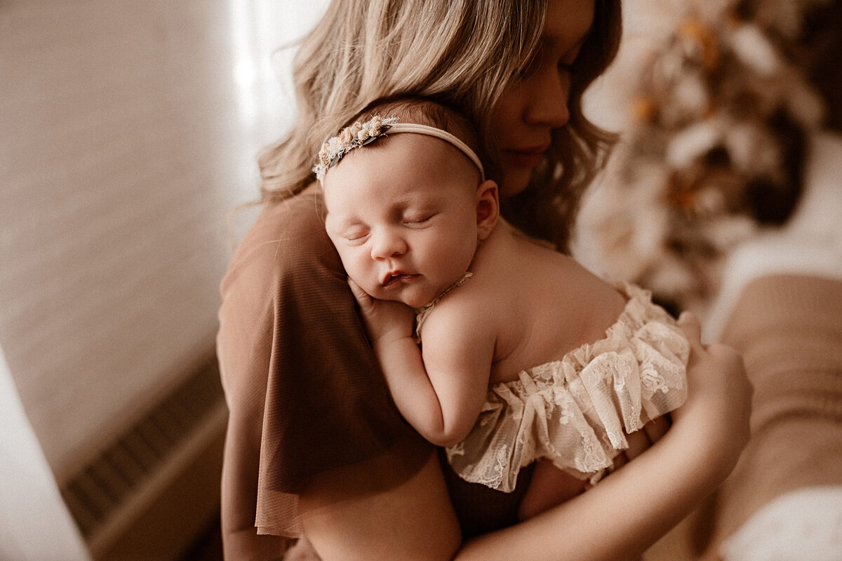 Mother holds her newborn baby boy while his older brother kisses his head.
