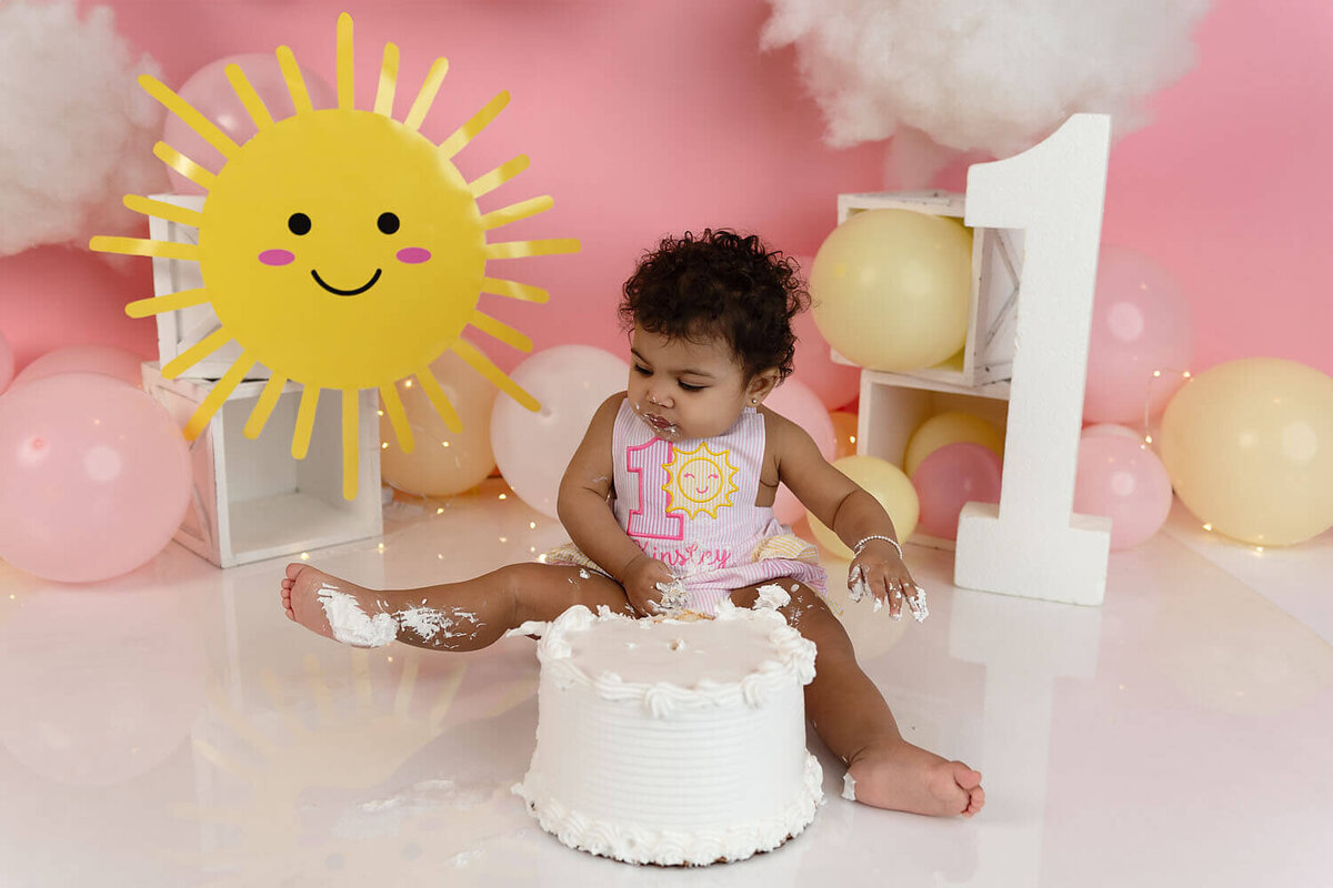 A happy toddler examines her frosting covered leg while smashing a cake in a studio