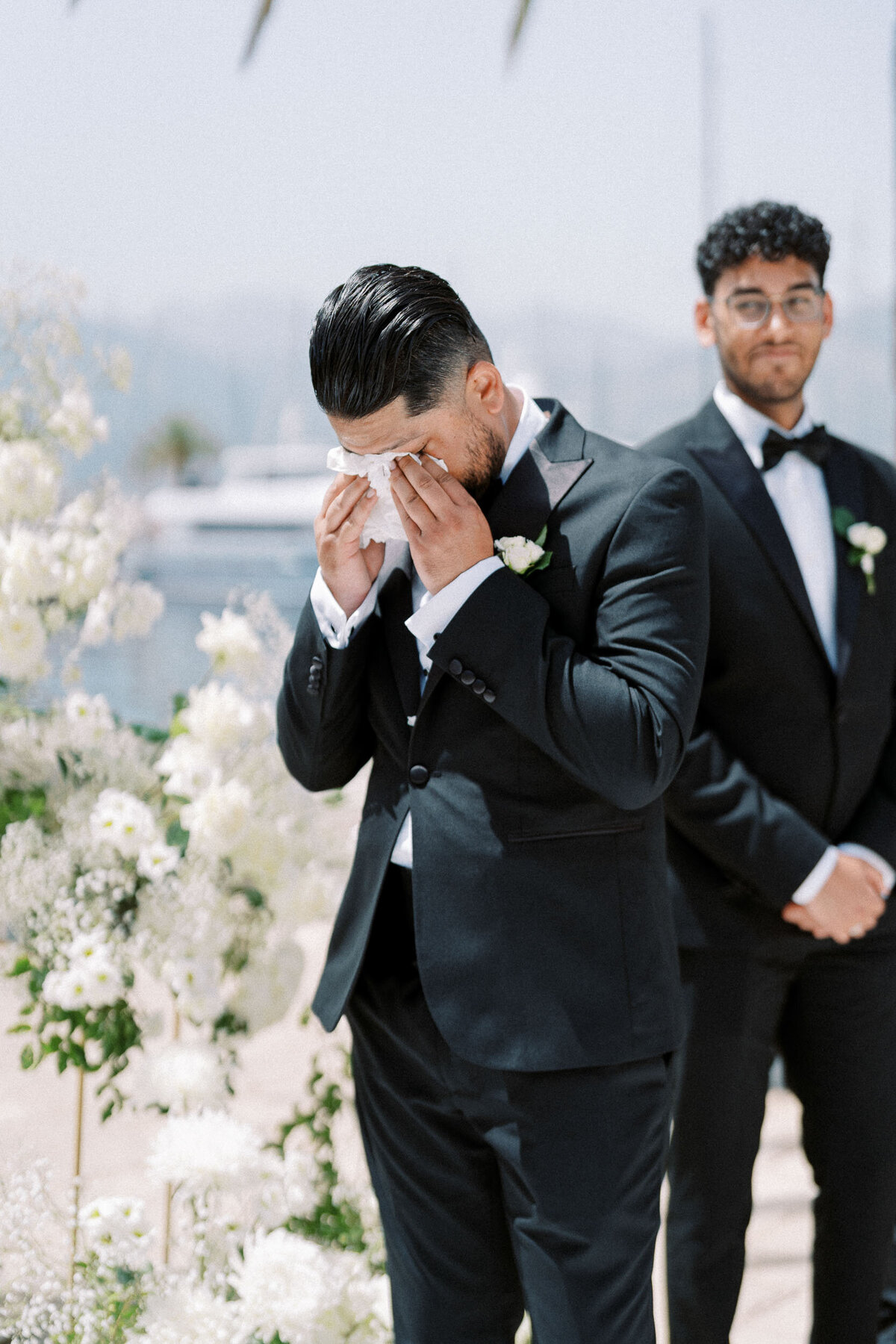 Groom wiping tears during a heartfelt wedding ceremony, captured in a candid documentary style by Nadtochiy Photography