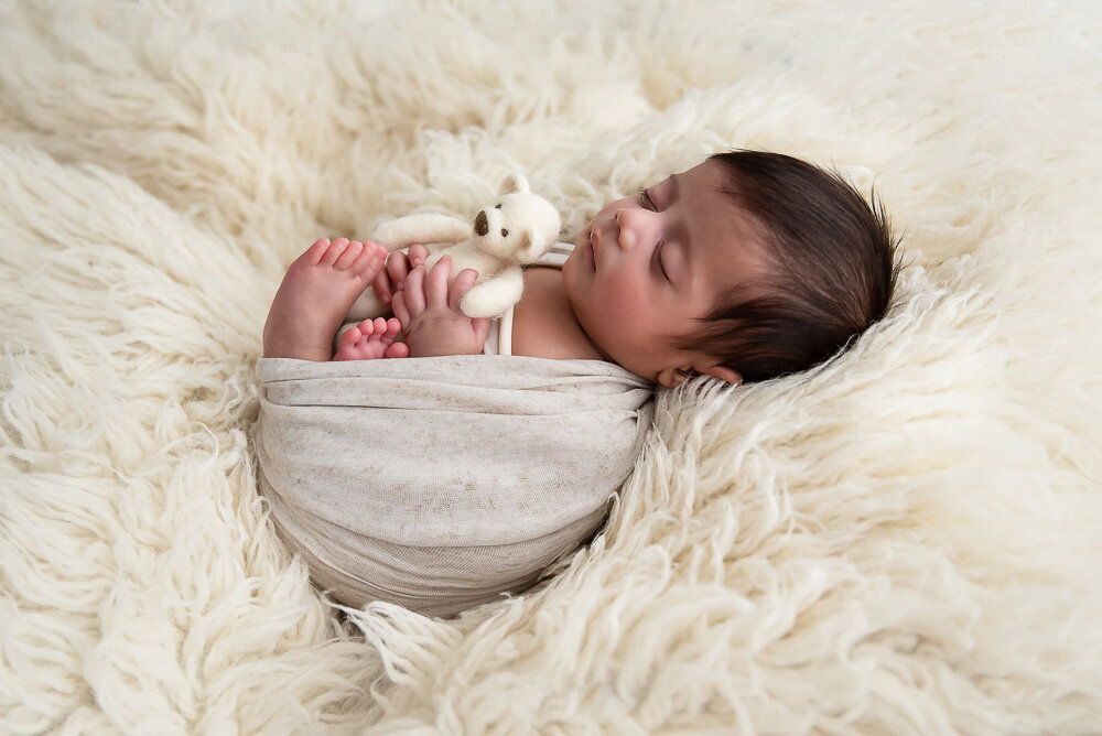 baby boy wrapped in beige on a cream rug.