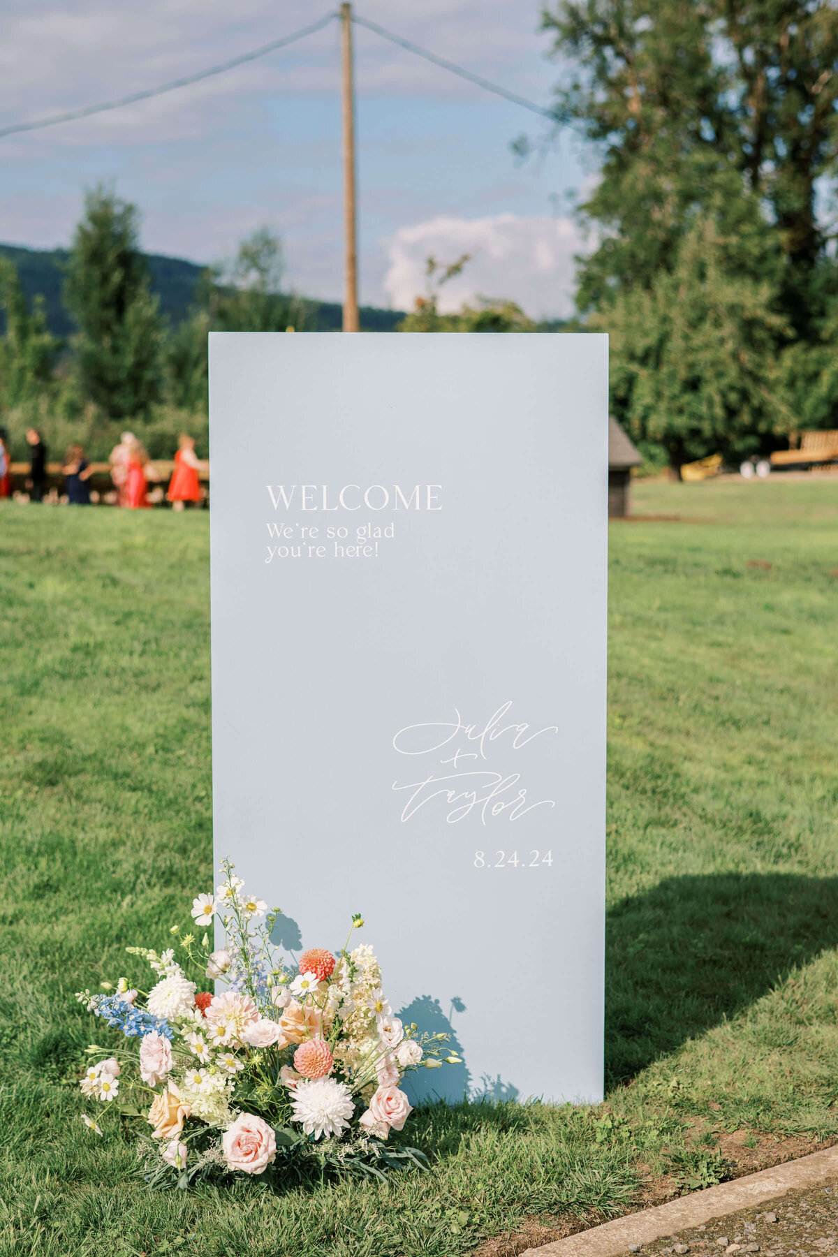 A welcome wedding sign with a flower arrangement in front of it at a luxury outdoor wedding.