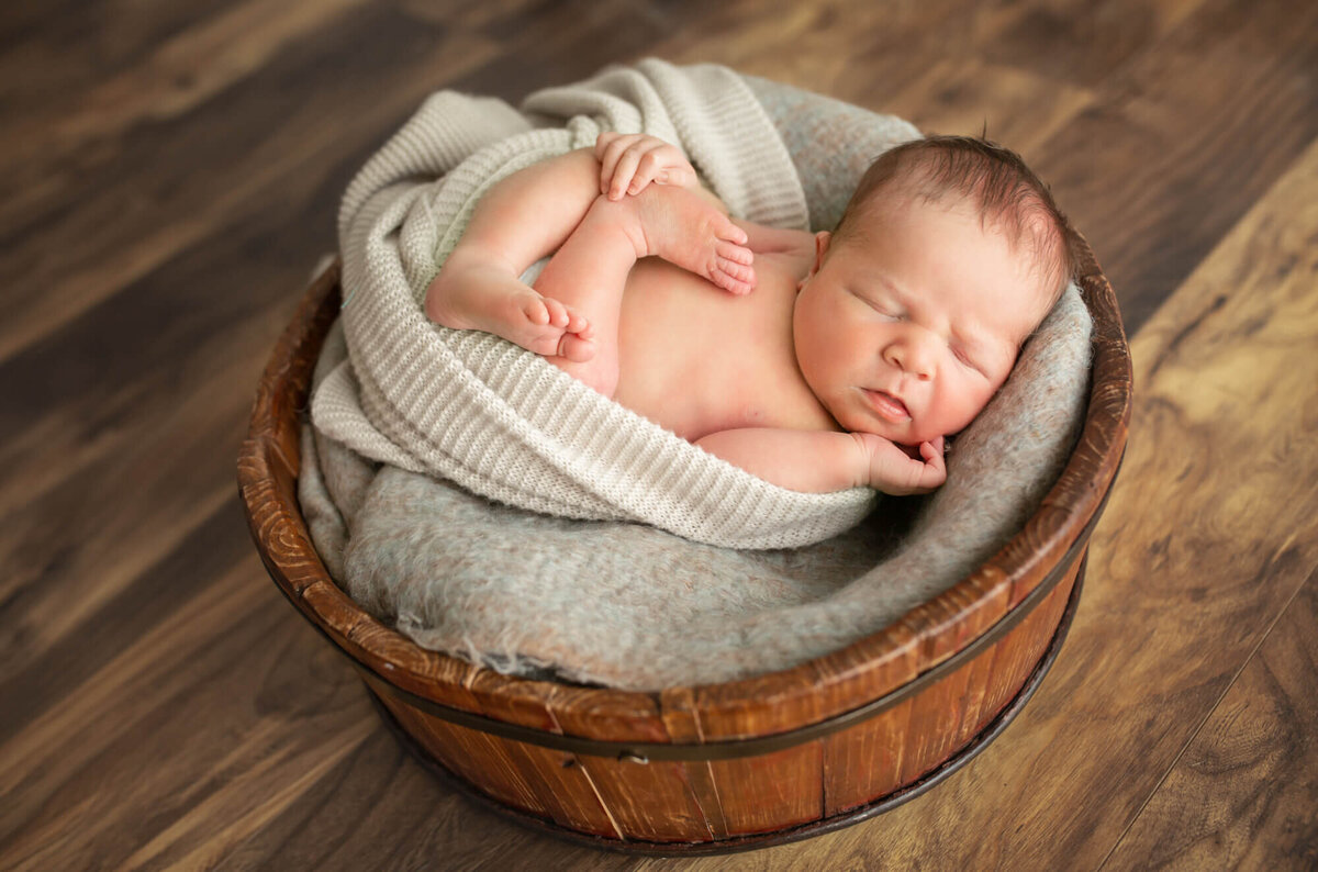 A newborn baby boy wrapped in a blanket sleeps in a wooden basket