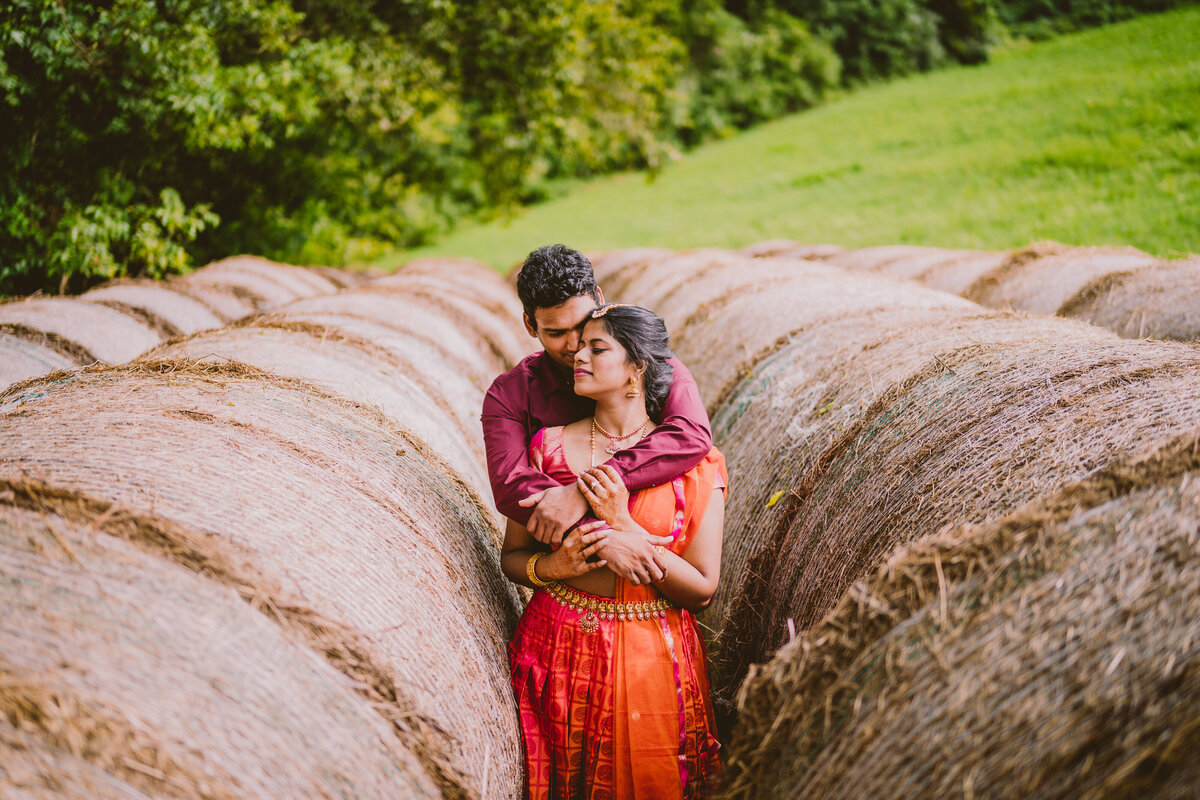 Engaged couple embracing in between hay bales at the natural lands stroud preserve in west chester pennsylvania
