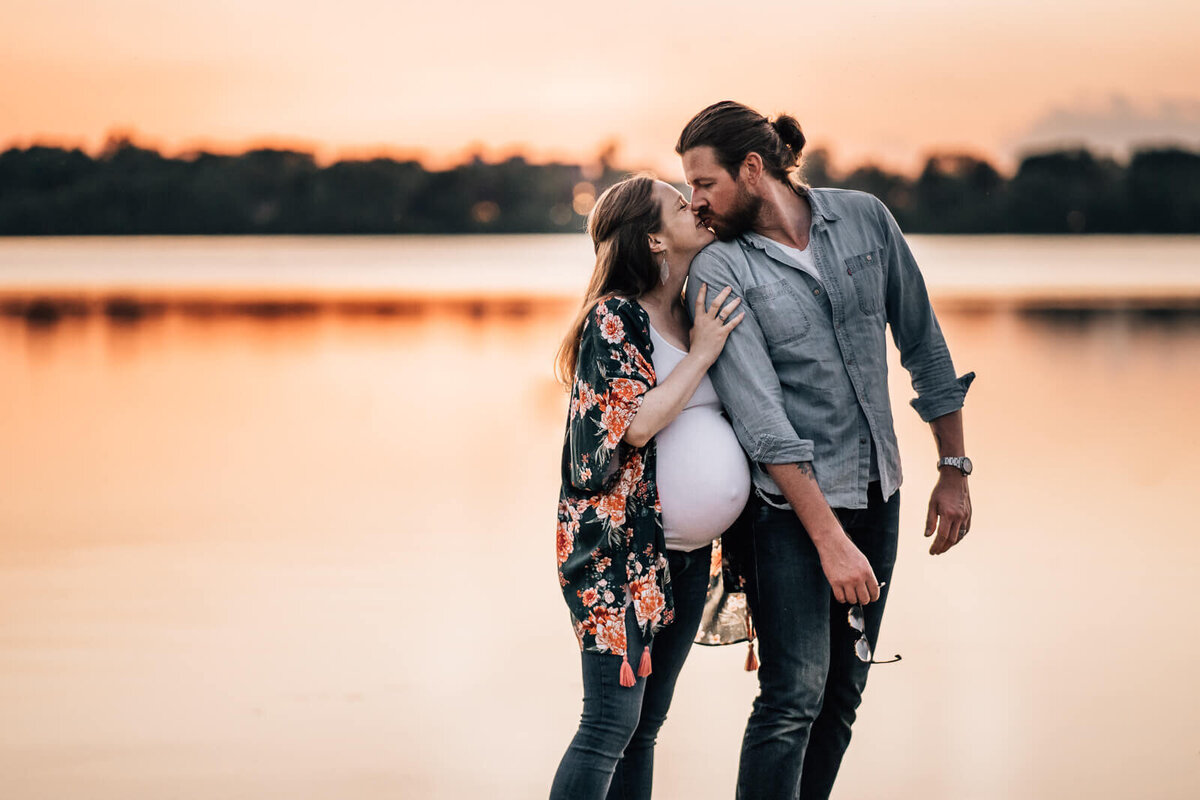 A couple expecting their first child kisses at Lake Harriet South Beach in Minneapolis during a sunset maternity photography session.