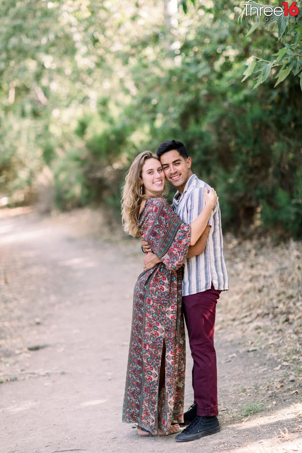 Engaged couple cozy up to each other as they pose for photos on a trail at the Frank G Bonelli Park in San Dimas, CA