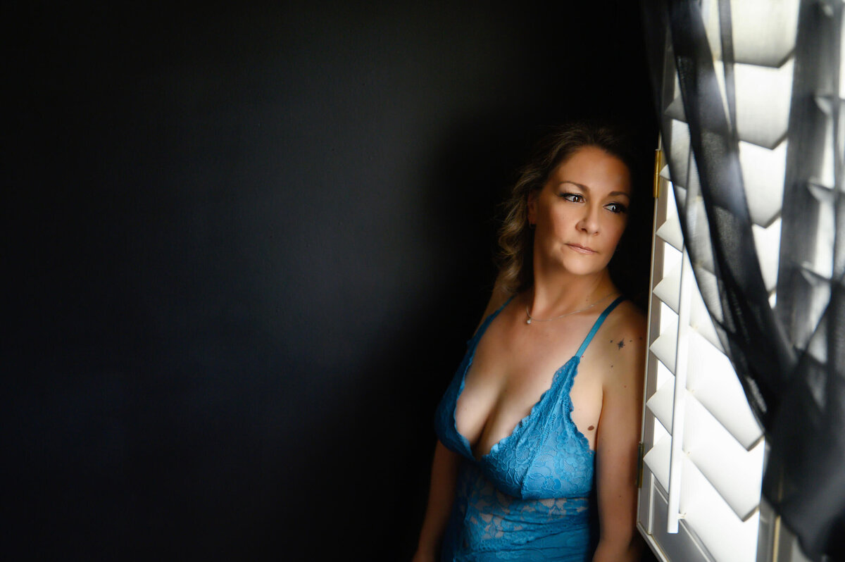 Lady staring out the window in blue lingerie for her Toronto boudoir photos.