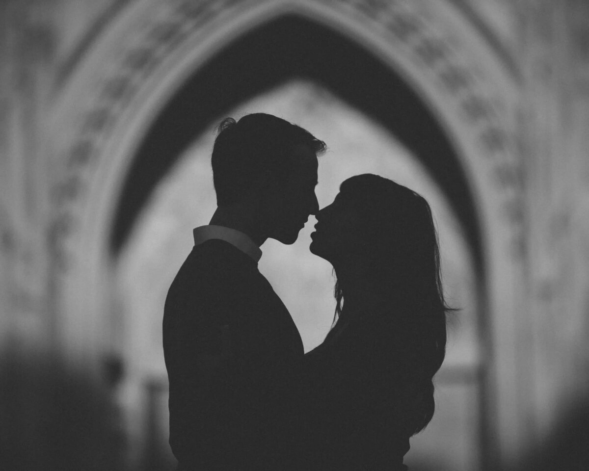 Silhouetted couple sharing an intimate moment in a gothic archway, with the image focused on their profiles