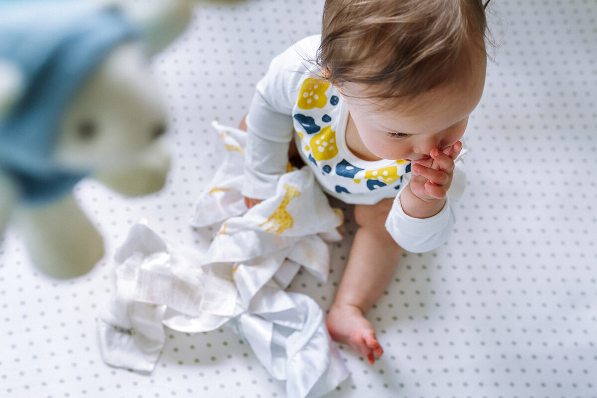 baby in crib sucking her thumb and holding on to her blanket with part of mobile in the foreground