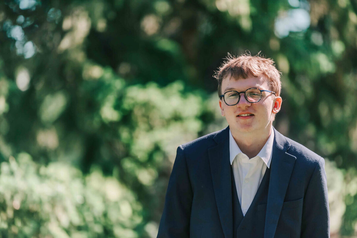 A handsome young man standing by some trees.