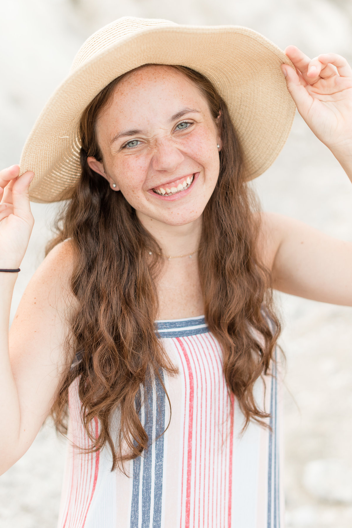 Senior girl smiling at camera and holding the brim of her summery hat.