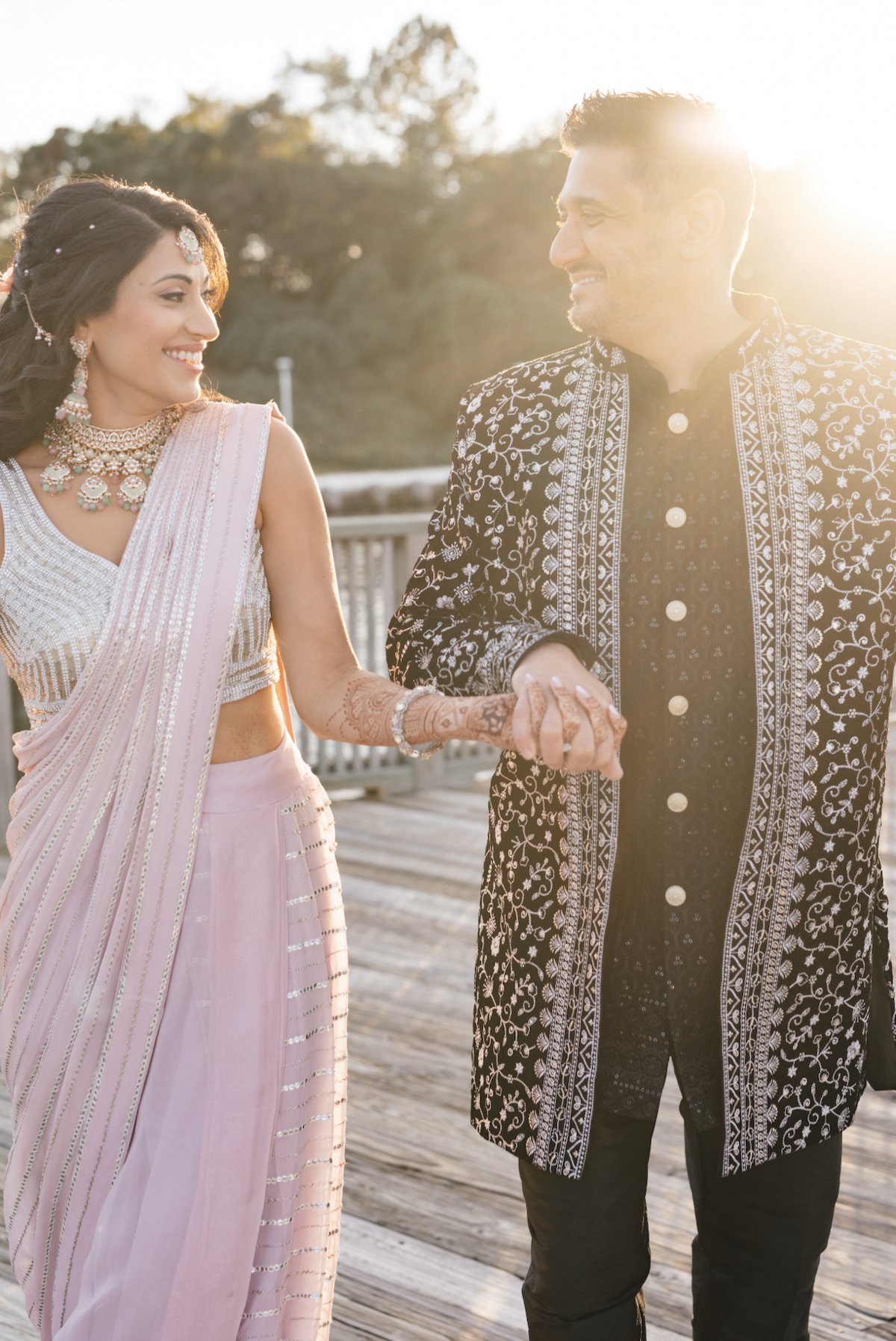 Bride and groom walking hand-in-hand at sunset in traditional South Asian outfits during their wedding portraits.