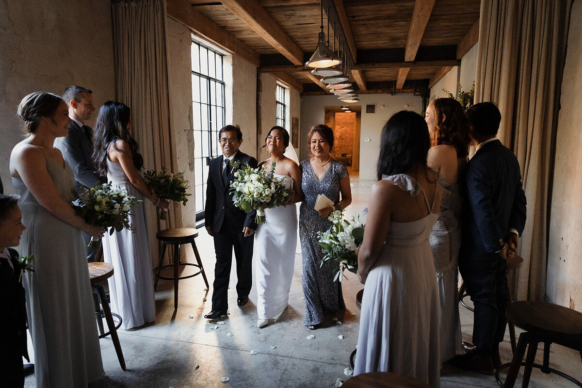 bride walking down the aisle escorted by her parents and she is crying