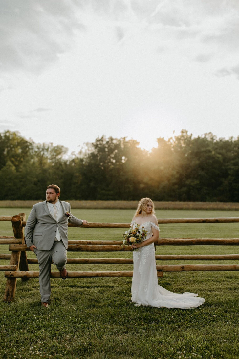 Bride and groom posing by a wooden fence at sunset