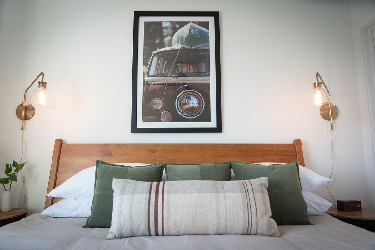 wood bedframe with green and plaid pillows and a wall mounted light on either side