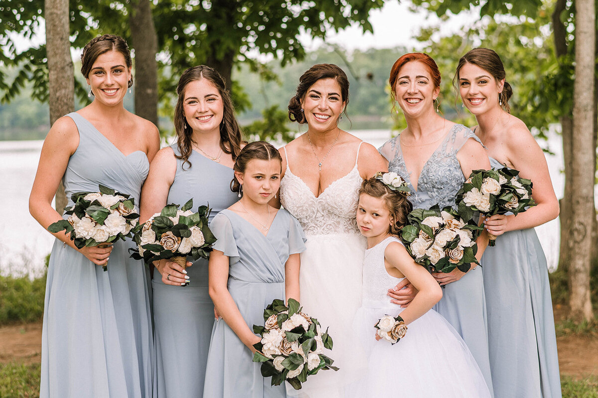 A bride standing in front of a lake surrounded by four bridesmaids and two flower girls in Sterling Virginia