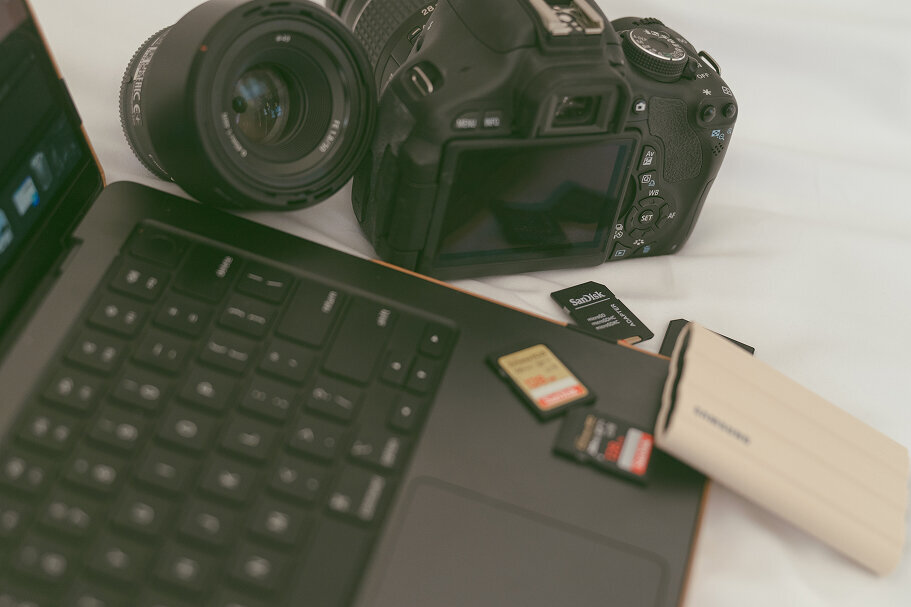 Close up detail shot of Michaela's keyboard on her laptop, a few SD cards, her camera, a lens, and a battery pack.