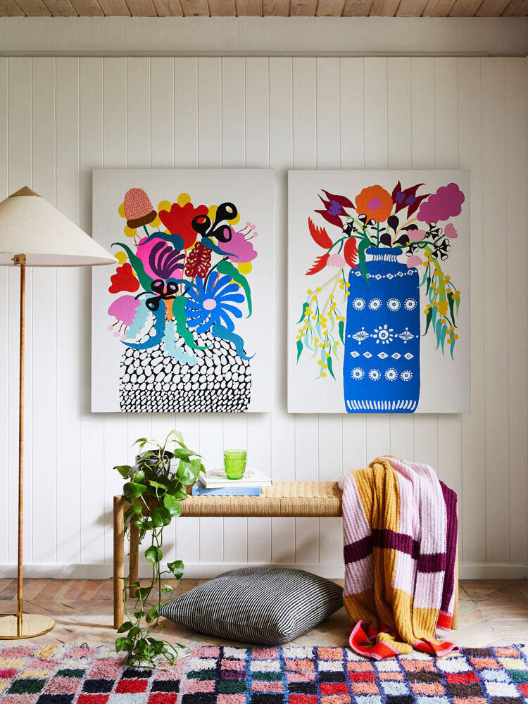 Bold floral artwork and round mirror styled in an entryway with patterned wallpaper and timber bench