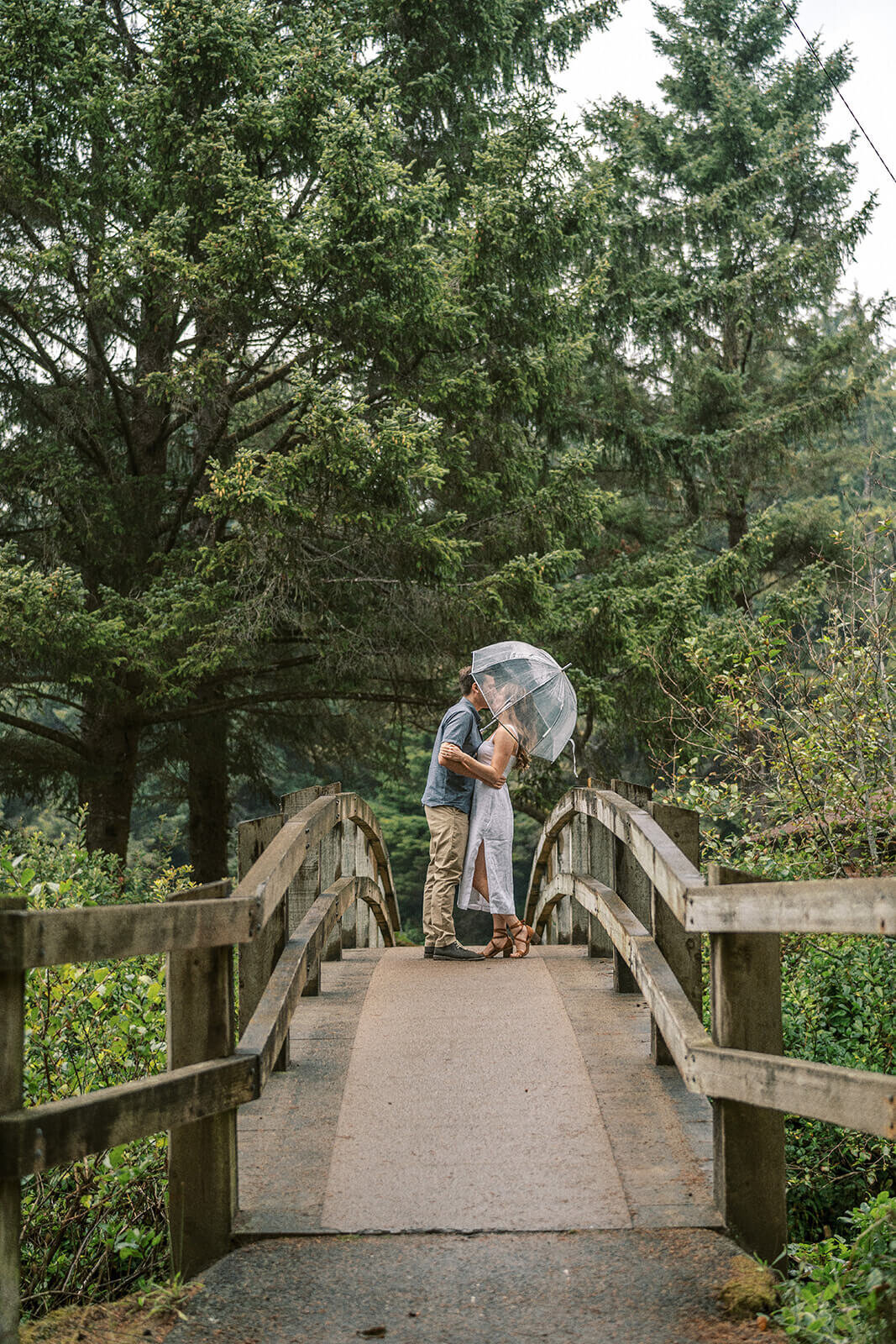 A couple walking on a bridge sharing an umbrella. 
