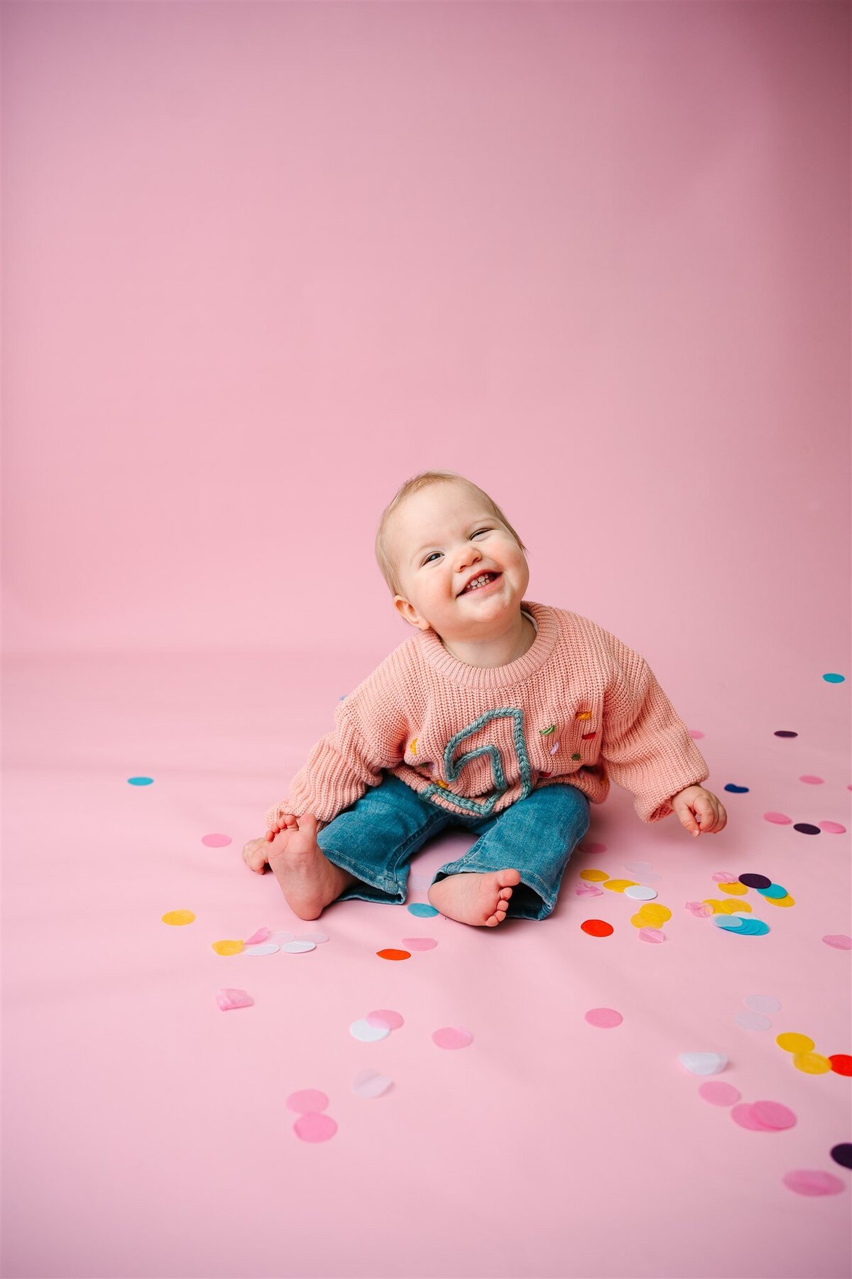 A baby sitting and smiling with confetti around them 