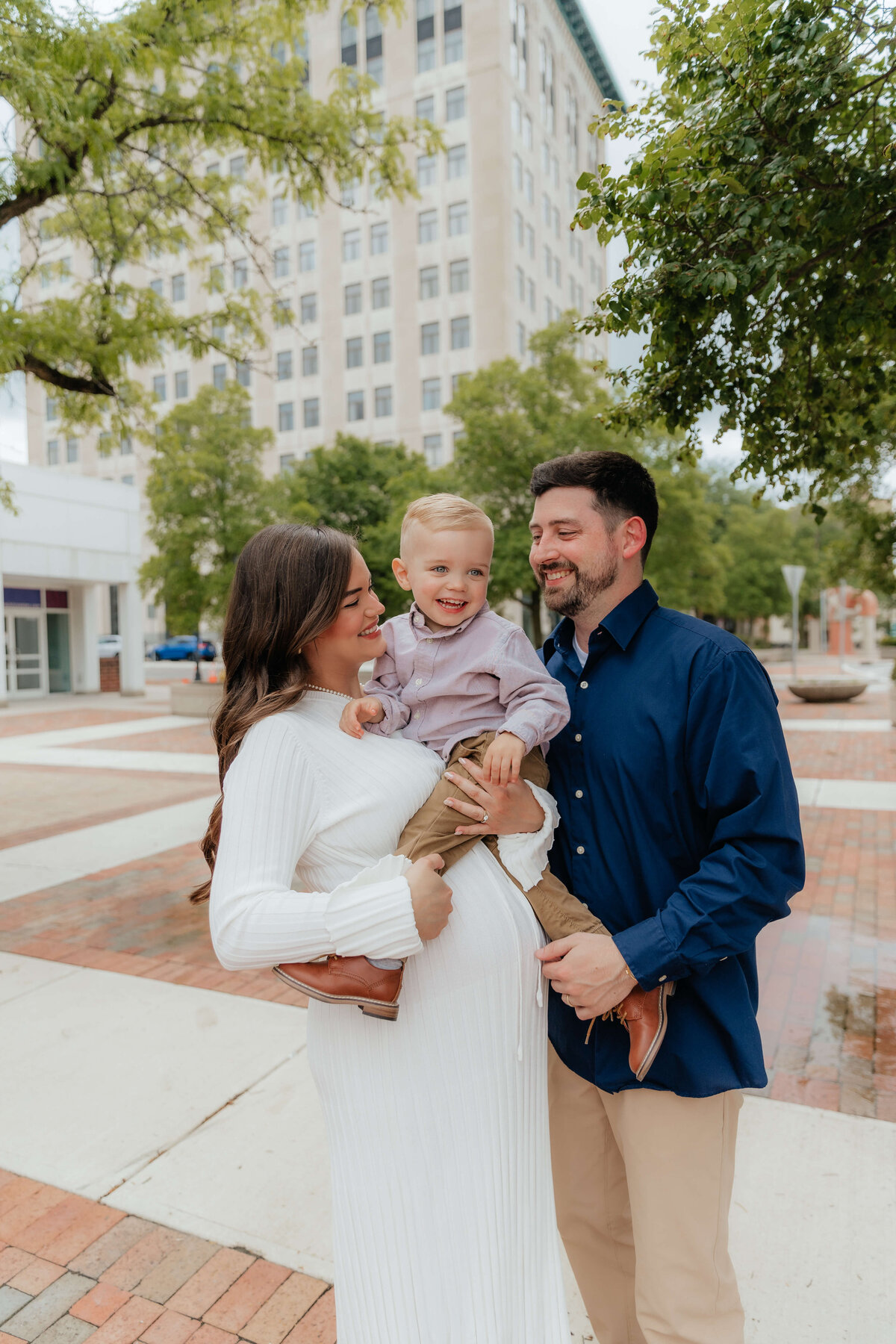 Smiling family with toddler during maternity shoot in city, lifestyle family photography in Michigan for parents who want joyful, candid moments