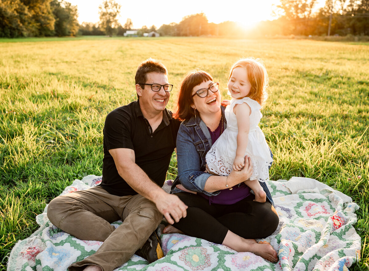 A happy family of three enjoying a moment together on a blanket in a sunlit field