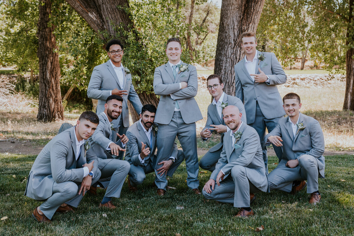 Groom and groomsmen give the camera a band pose while smiling at camera.