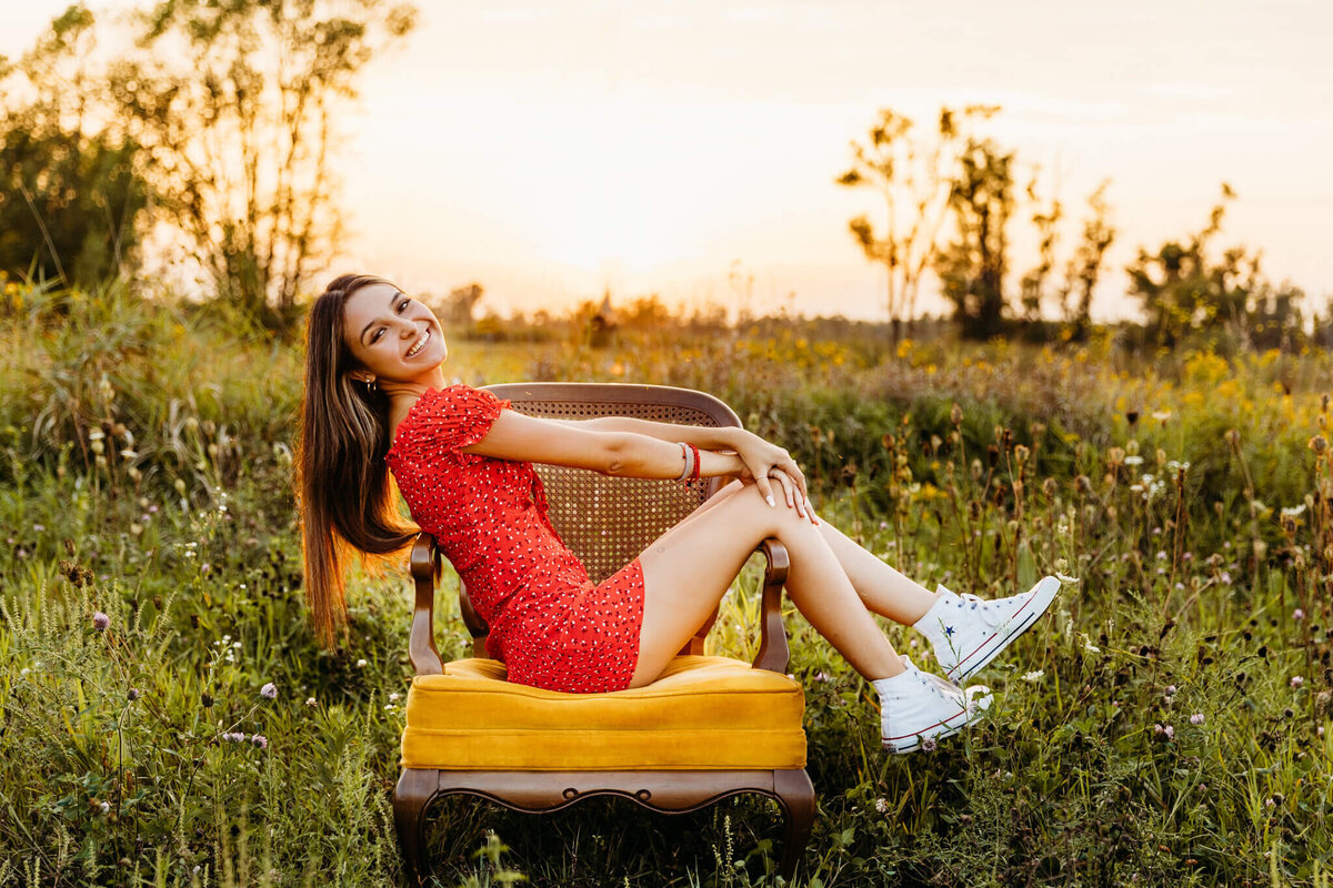 high school girl sitting on a chair in a field at sunset for senior photos