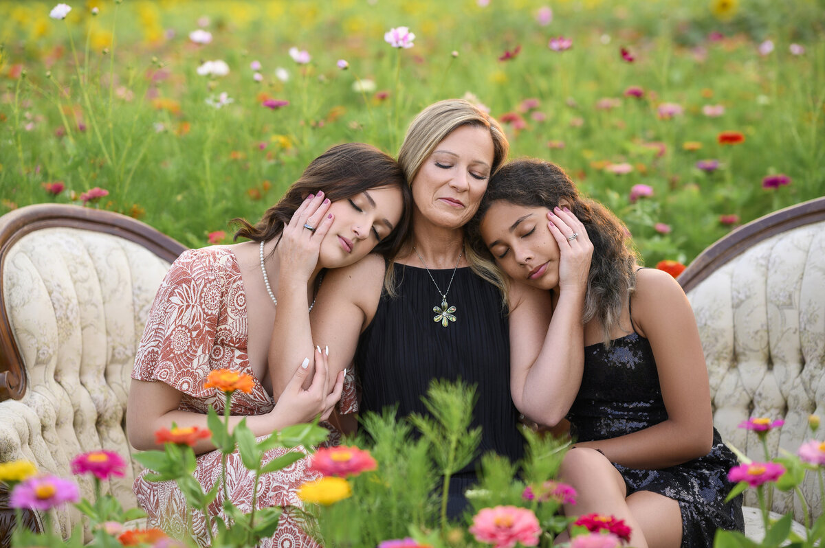 A mother and her two daughters resting on a vintage sofa, surrounded by colorful flowers