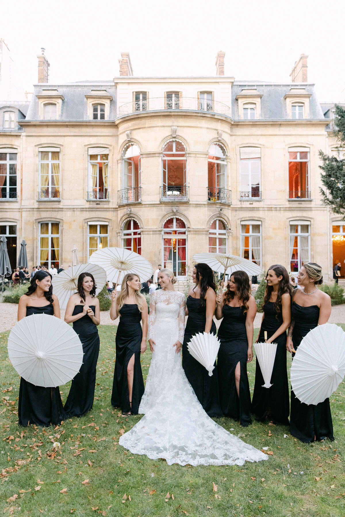 Bridal party laughing while holding white  summer umbrellas.