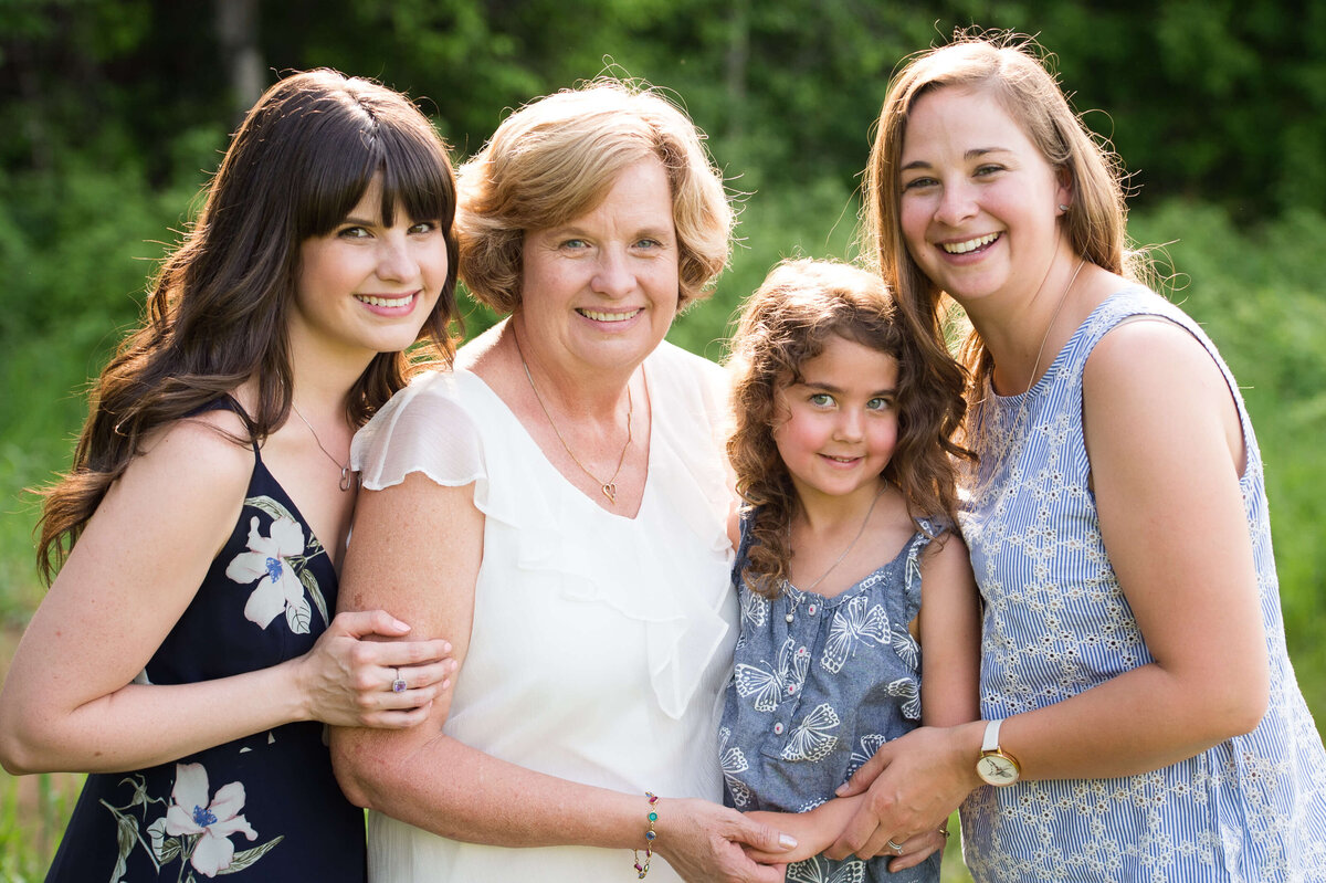 a photo of grandma with her adult daughters and granddaughter during her extended family session outdoors in a grassy filed captured by Ottawa Family Photographer JEMMAN Photography
