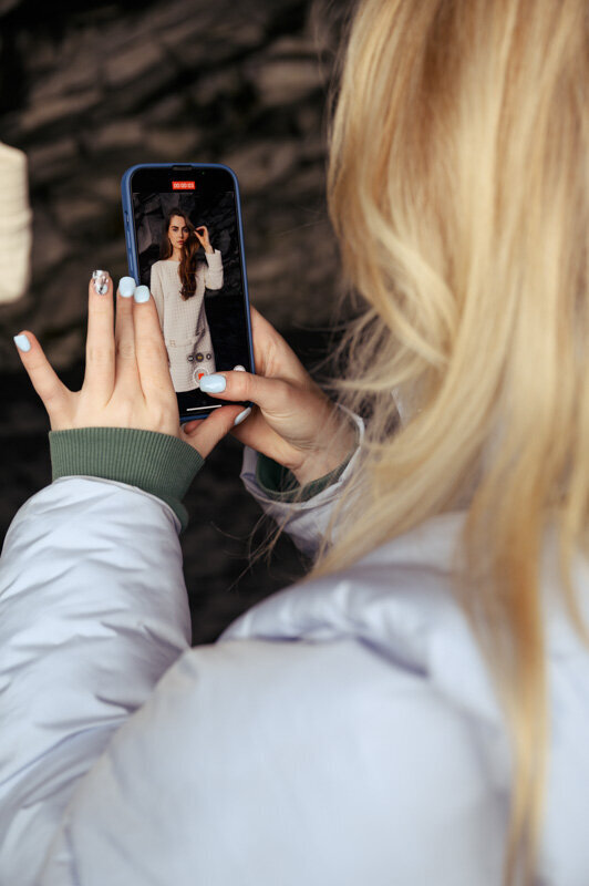 A blonde female is making an iPhone video of a model in a dress in Iceland