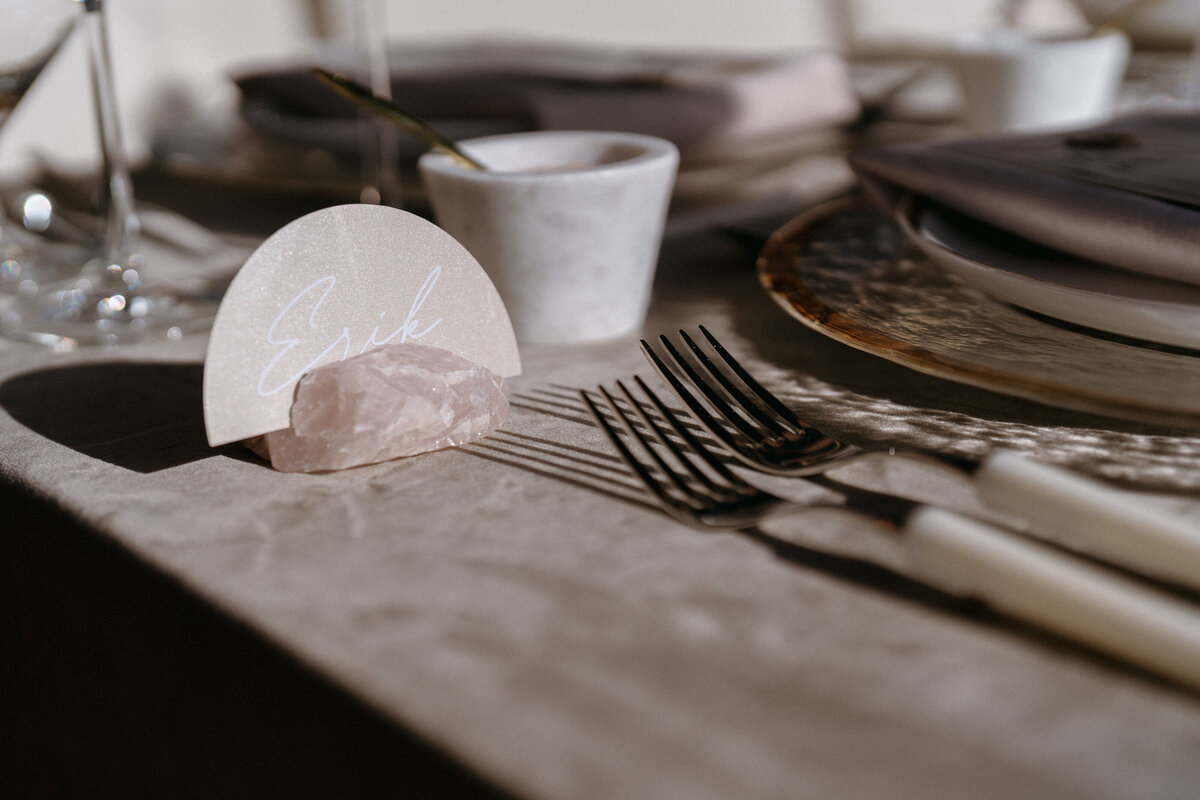 Modern wedding place setting with crystal name card holder, gold flatware, and neutral-toned linens