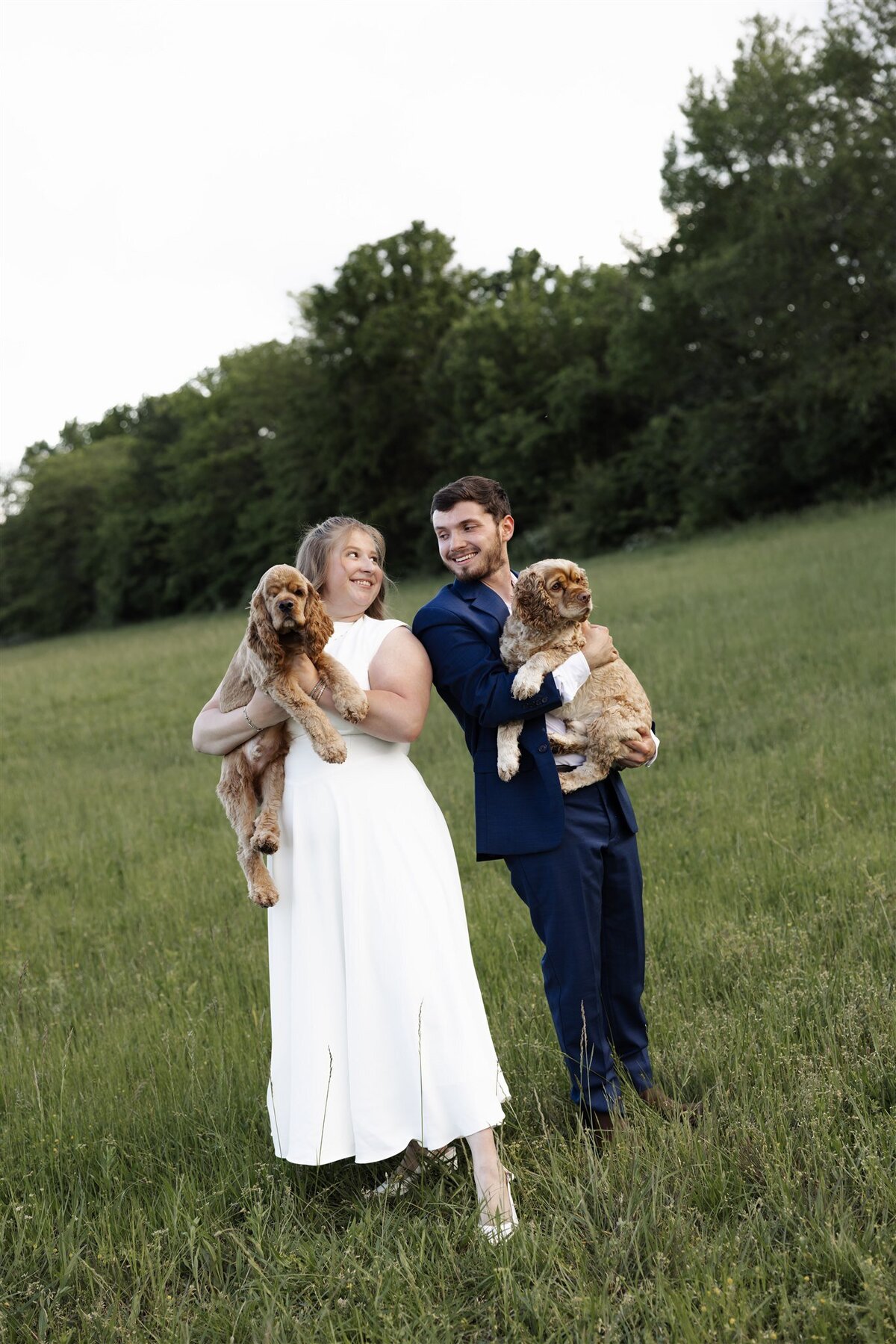 bride and groom holding dogs in grassy field