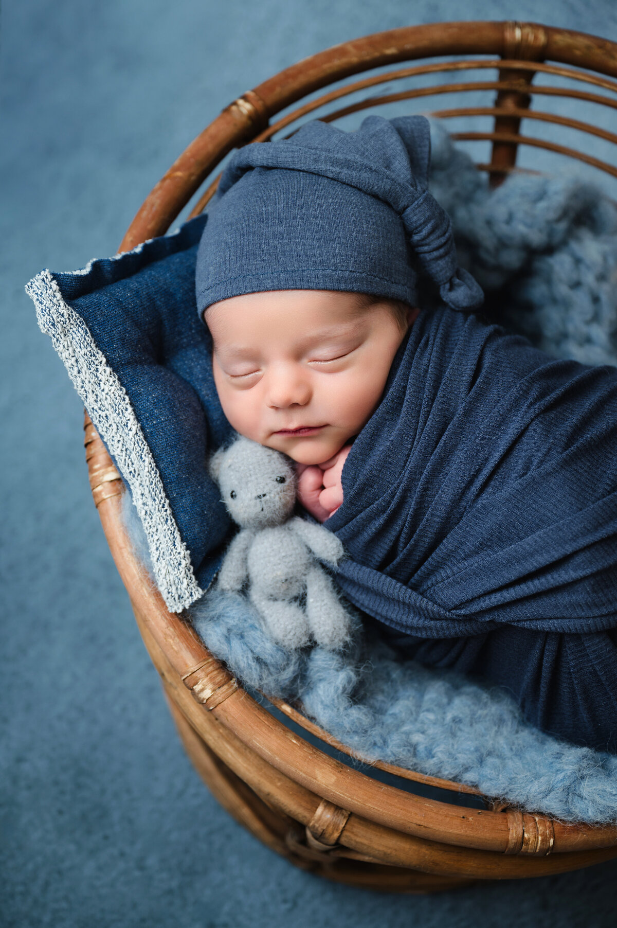 This sweet newborn photography session in Pittsburgh features a baby boy peacefully swaddled in a soft blue wrap, resting in a wicker basket. The neutral tones and soft textures highlight the serene beauty of a newborn’s first portrait.