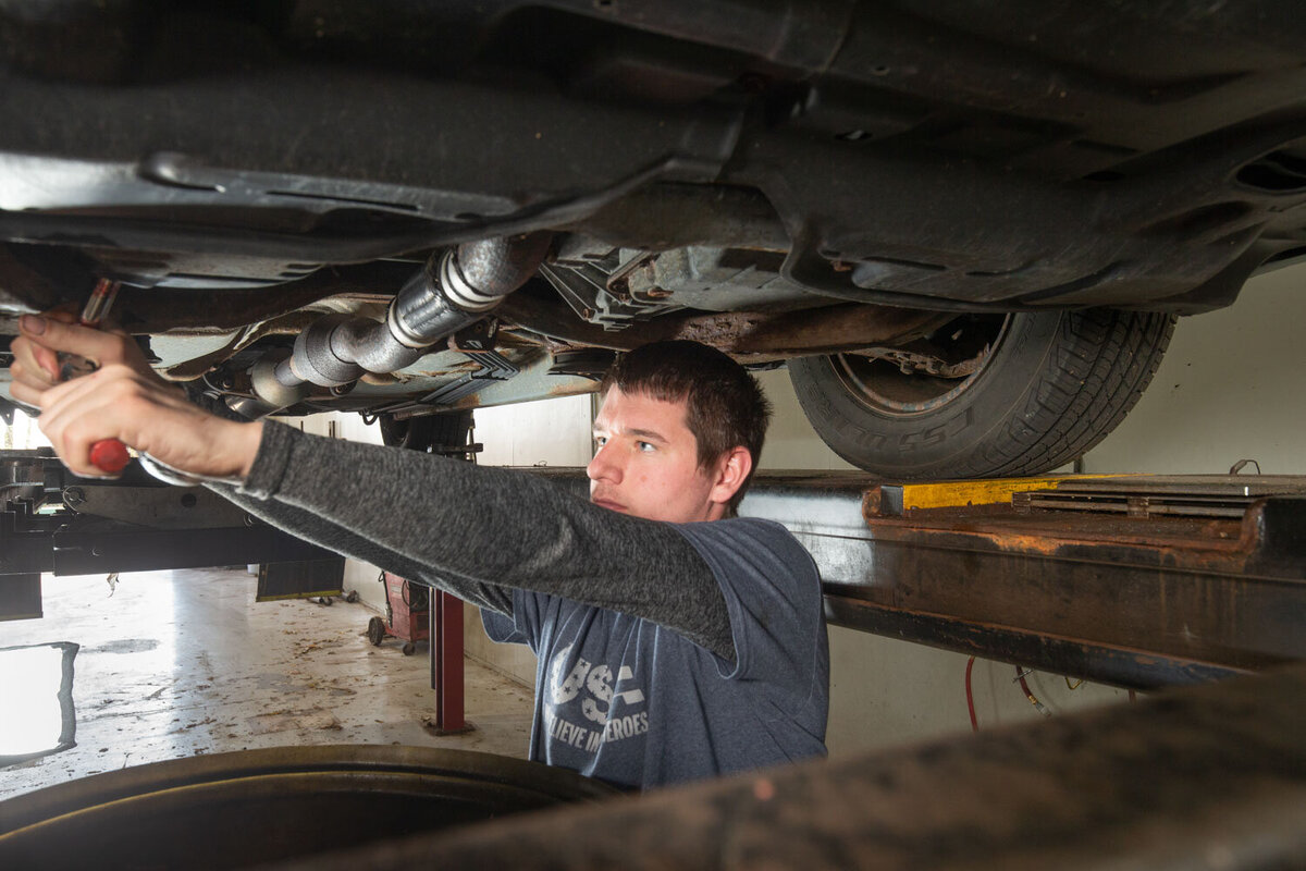 A man is working under a car wearing a shirt