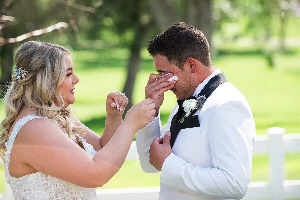 A bride wipes the tears from her groom as he reacts to seeing her for the first time on their wedding day.