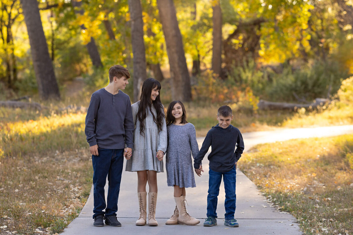 four siblings holding hands standing on a path laughing