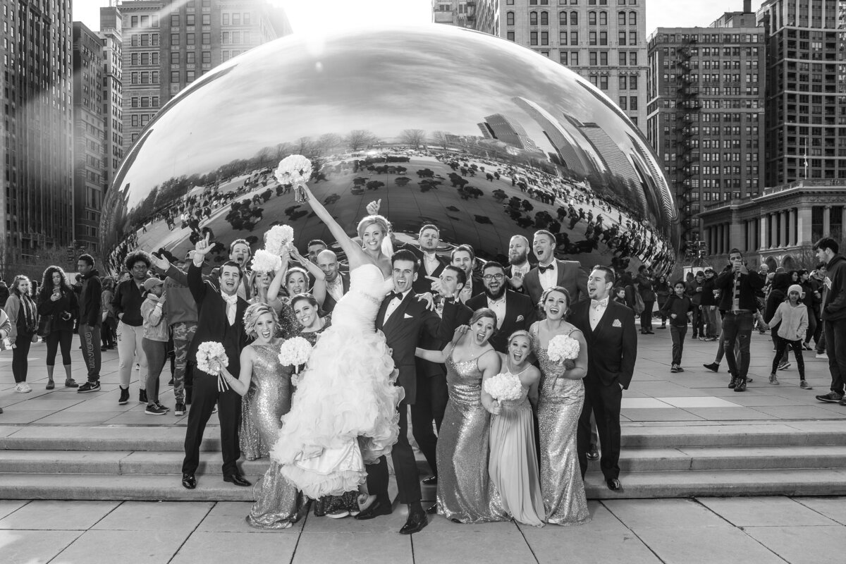 Groom picking up the bride for a fun shot of a bridal party in front of the Bean at Millennium Park.