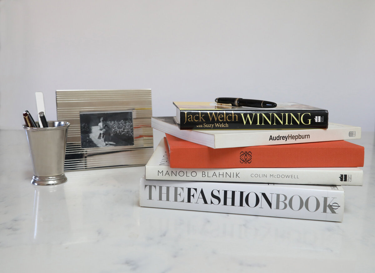Pile of fashion books on a table next to a pen cup and photograph