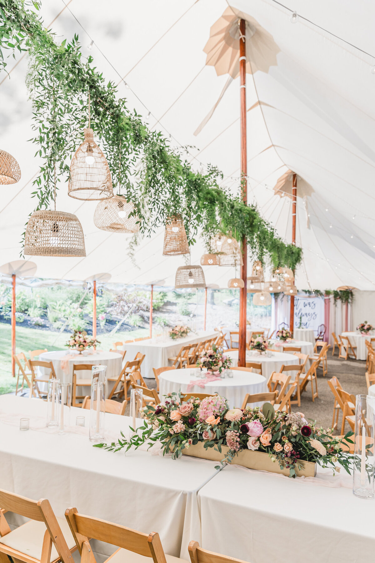 A garden wedding reception under a sail cloth tent  with hanging vines an rattan lanterns