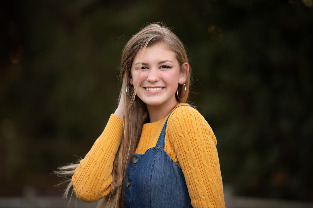 A teenage girl wearing a yellow sweater and denim dress smiles in a Dallas family portrait session, captured by a Dallas family photographer.