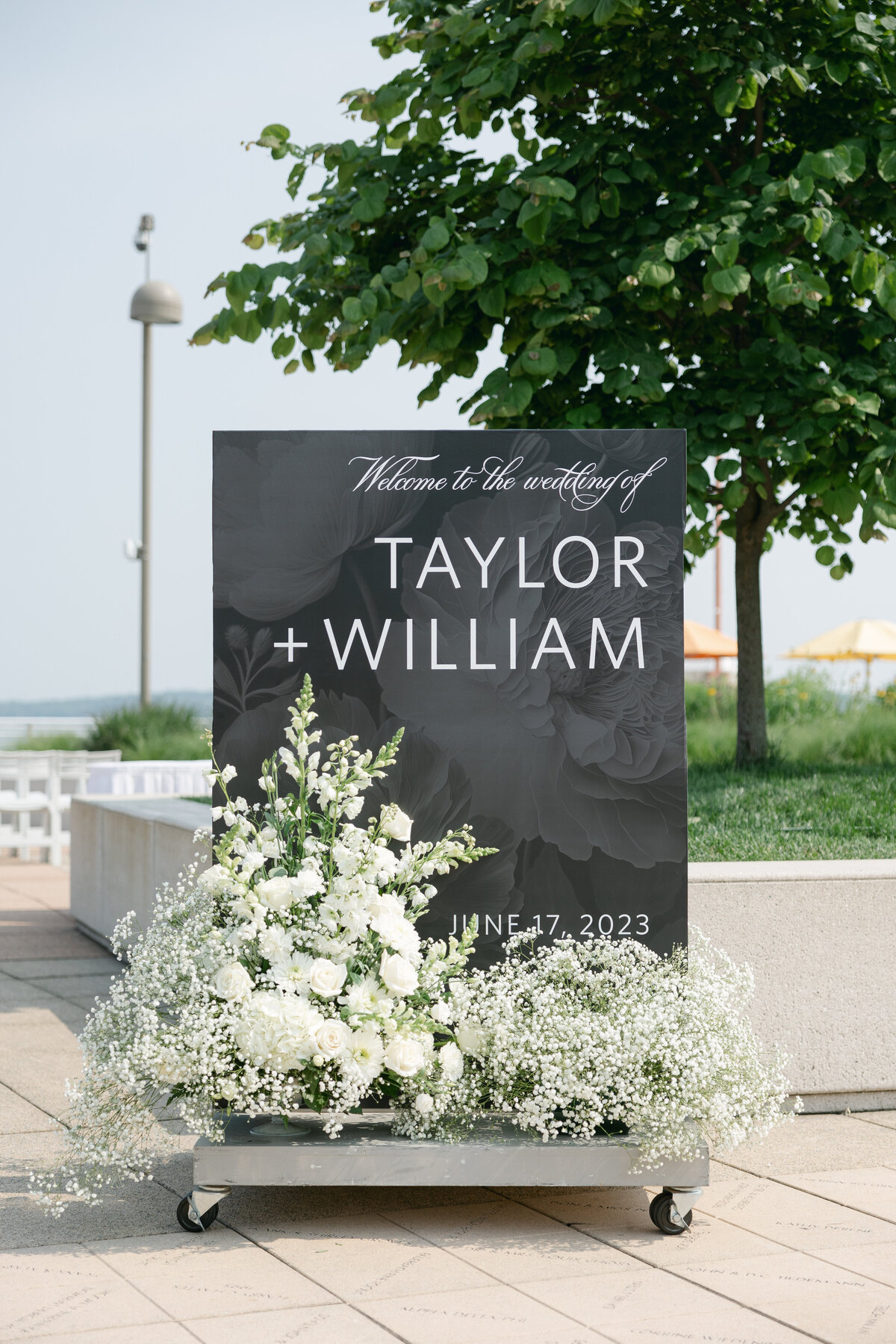 A beautifully styled ceremony welcome sign on the rooftop of Monona Terrace, adorned with overflowing florals that create a stunning backdrop for the wedding celebration.