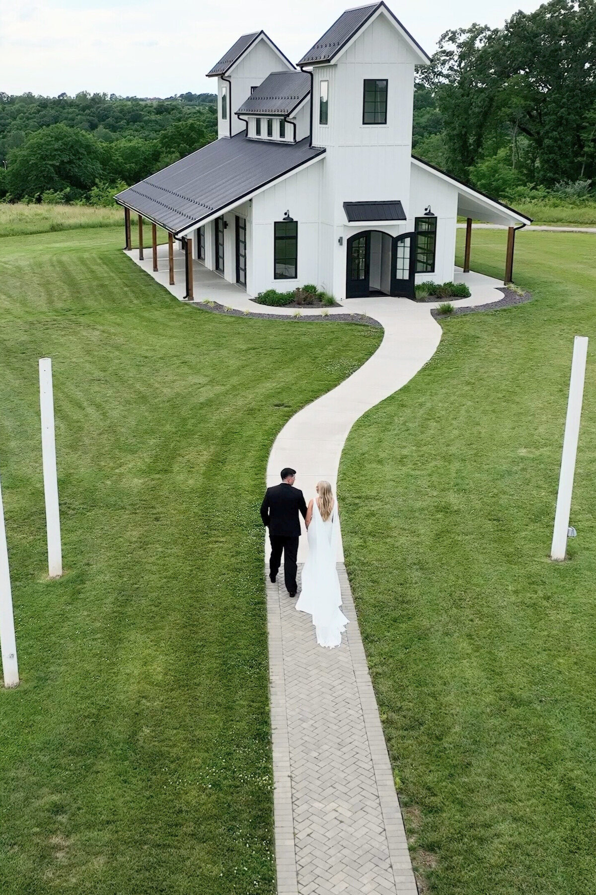 Aerial shot of bride and groom walking towards chapel captured by drone at The Brim