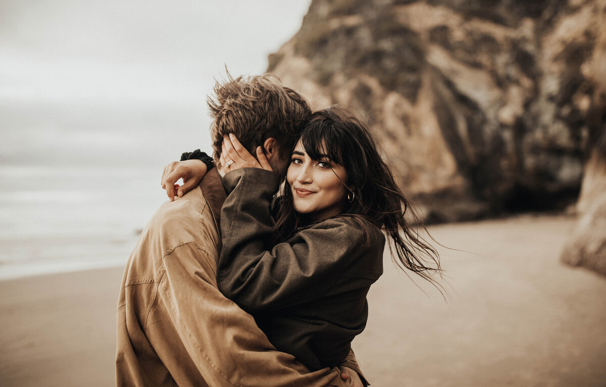 Woman looking at camera while hugging man on beach